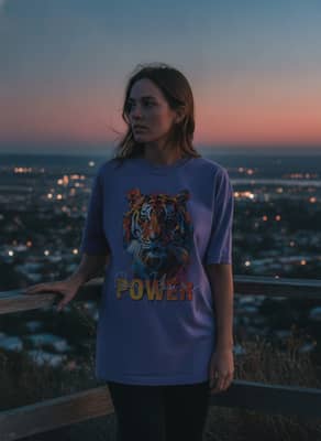A person in a violet tiger graphic t-shirt stands at a hilltop overlook at sunset.