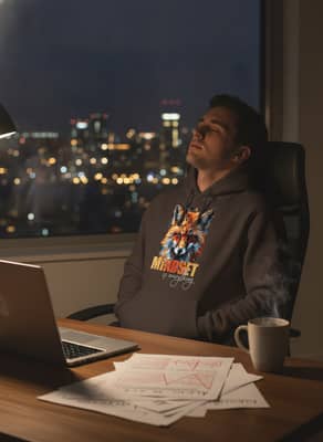 A person wearing a dark chocolate fox print hoodie sits at a dimly lit desk reviewing a printed draft.