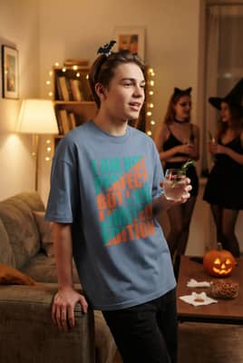 A person wearing a dark graphic t-shirt and a bat hair clip leans against a couch while holding a sparkling mocktail.