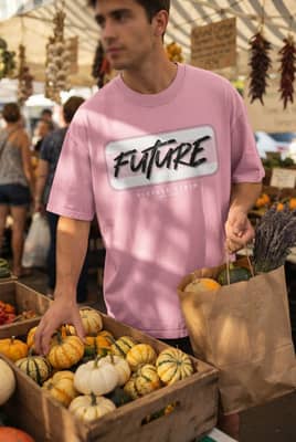 A person wearing a denim-look T-shirt holds a paper bag while choosing small pumpkins at a market stall.