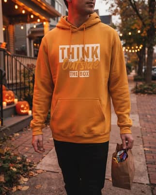 A person in a gold hoodie carries a small candy bag past porch jack-o'-lanterns at dusk.