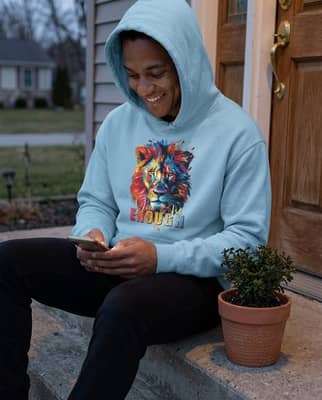 A person wearing a hoodie sits on a front porch step at dusk, smiling while reading their phone.