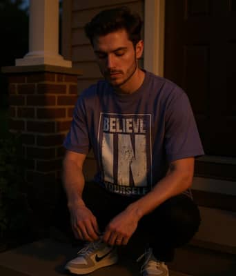 A person in a graphic tee sits on a porch step at dusk, lacing sneakers, with soft golden light on the sleeves.