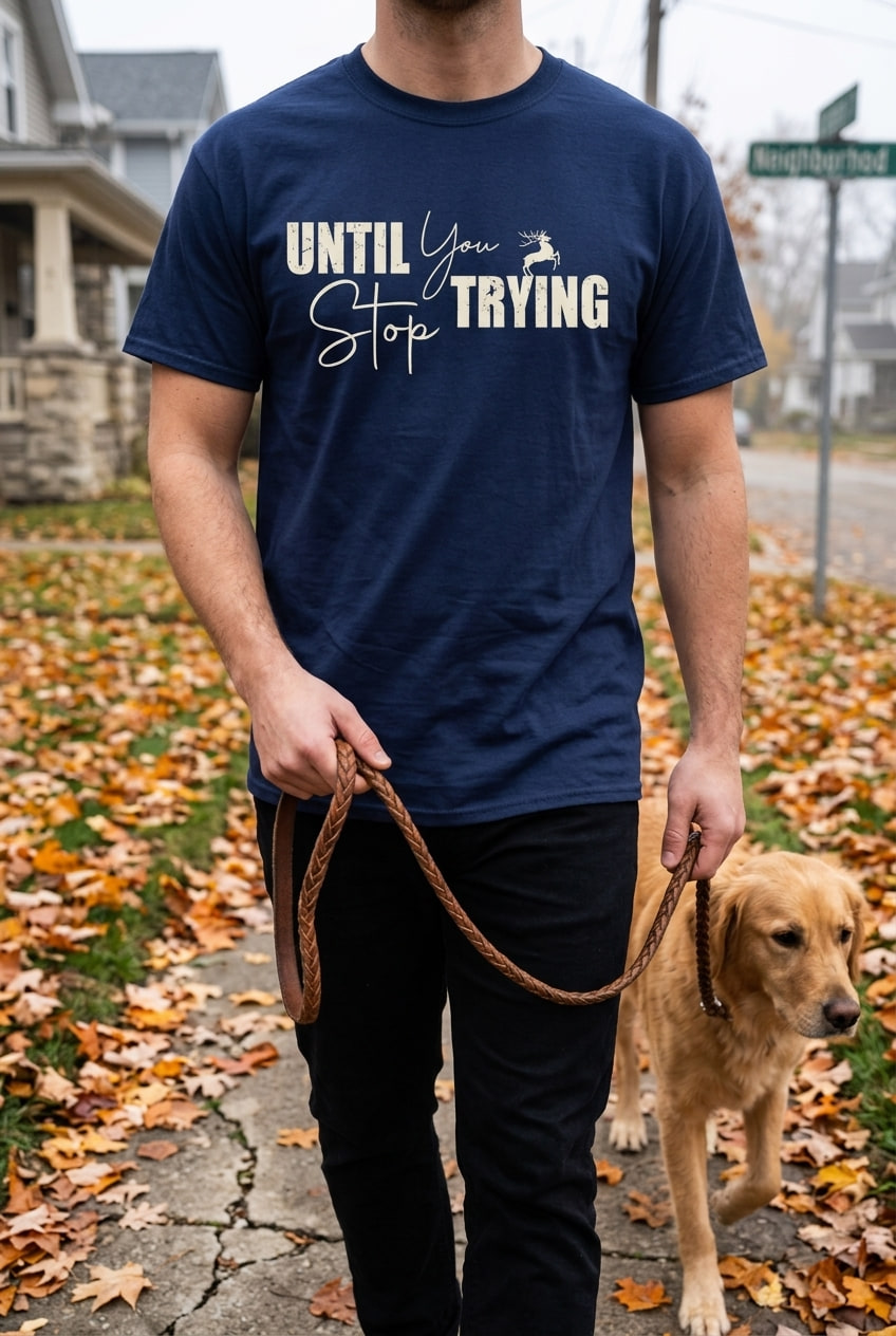 A person in a navy blue t-shirt walks a dog along a sidewalk covered in fallen autumn leaves.