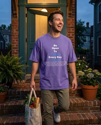 Man in his early thirties carrying a bag of groceries up brick porch steps wearing a violet t-shirt.