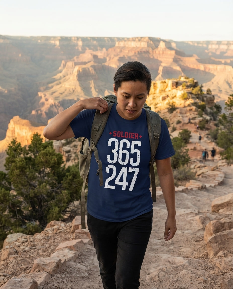 A person in a Caution Godfather tee adjusts a backpack strap on a canyon overlook trail.